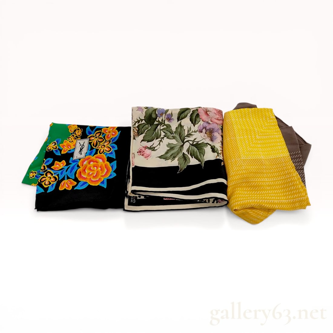 A Trio of Vintage Silk Scarves Including Two Yves Saint Laurent Examples: A trio of vintage silk square scarves, including two by Yves Saint Laurent and one of Japanese origin. Designs include a black ground with orange roses, a cream field with pink floral bouquets and bla