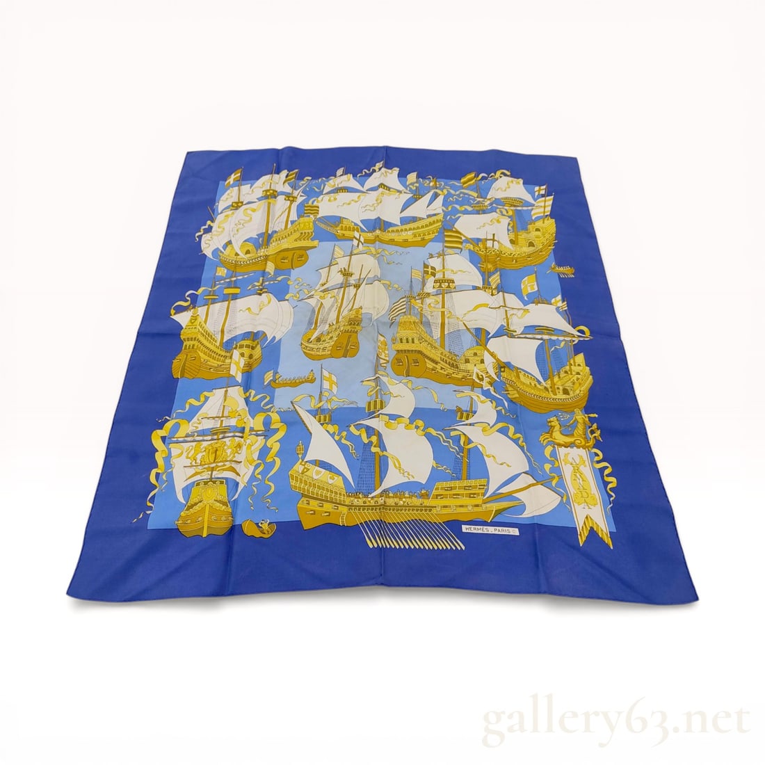 Herm?¨s Armada Silk Twill Carre 90: Hermès silk twill scarf in the Armada pattern, featuring a nautical theme of historic sailing vessels. The design is rendered in gold and white against a two-tone blue field with a wide royal b