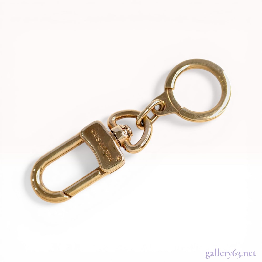 Louis Vuitton Goldtone Anneau Cles Key Ring: Louis Vuitton Anneau Cles key ring in gold-toned metal. The accessory features a spring-loaded snap-hook and a flat split ring joined by a central swivel link. The snap-hook is engraved with the Louis