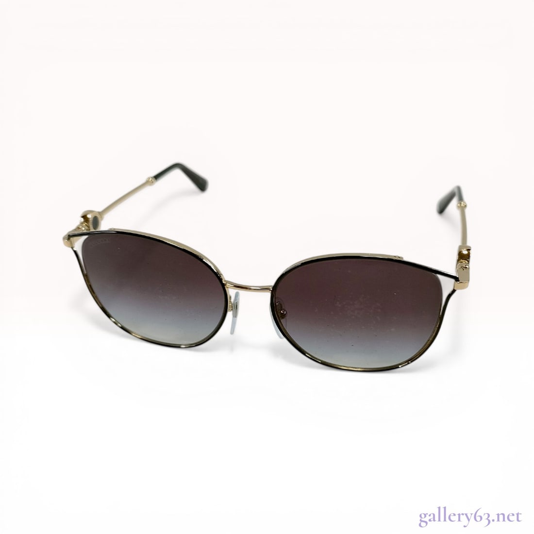 Bulgari Gold-Toned Metal Cat-Eye Sunglasses with Gradient Lenses: Bulgari designer sunglasses featuring a gold-toned metal frame in a rounded cat-eye silhouette. The gradient lenses transition from dark grey-brown to light blue-grey and feature an etched brand signa
