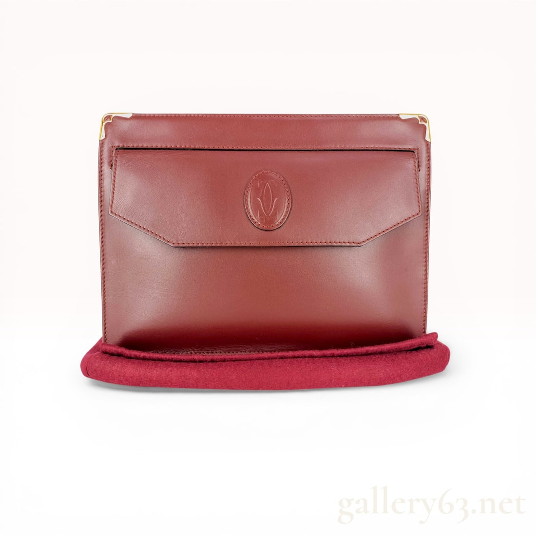 Must de Cartier Vintage Burgundy Leather Clutch: Must de Cartier vintage clutch crafted from smooth calfskin leather in the brand signature burgundy color. The front features a pointed flap pocket with an embossed interlocking C logo and gold-tone m