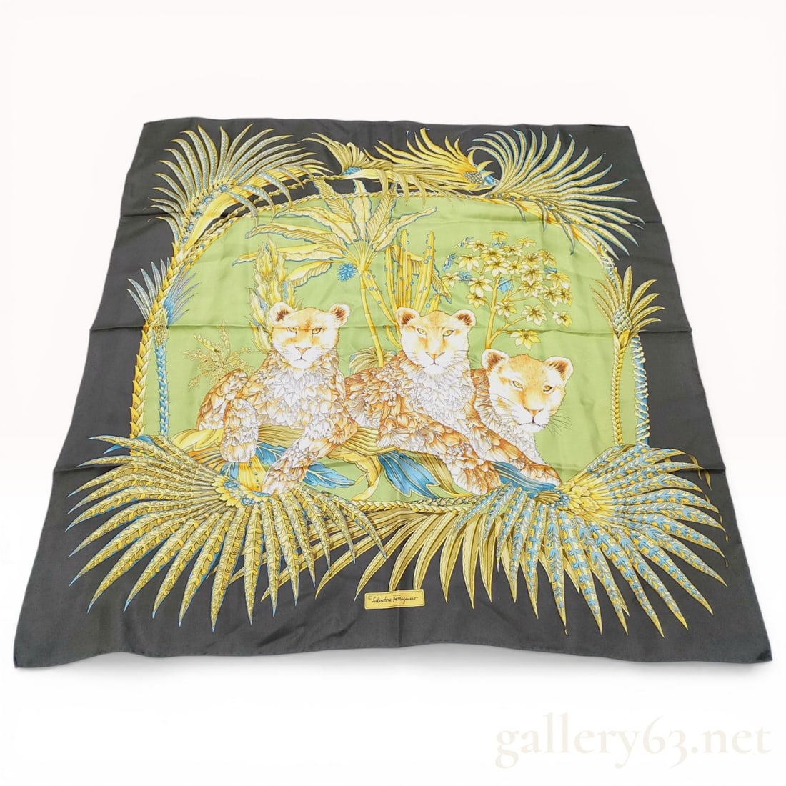 Salvatore Ferragamo Silk Scarf with Lion Cub Motif: Salvatore Ferragamo square silk scarf featuring a jungle themed illustration, made in Italy. The central light green panel depicts three lion cubs surrounded by tropical flora including palm fronds an