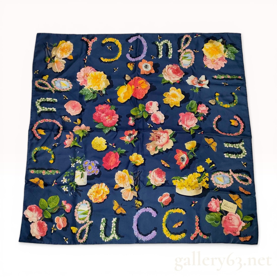 Gucci Navy Blue Silk Flora Botanical Scarf with Floral Lettering: Gucci silk scarf featuring a botanical flora print on a navy blue ground. The design includes various flowers, butterflies, and bees, with the Gucci name spelled out in floral-motif letters along the