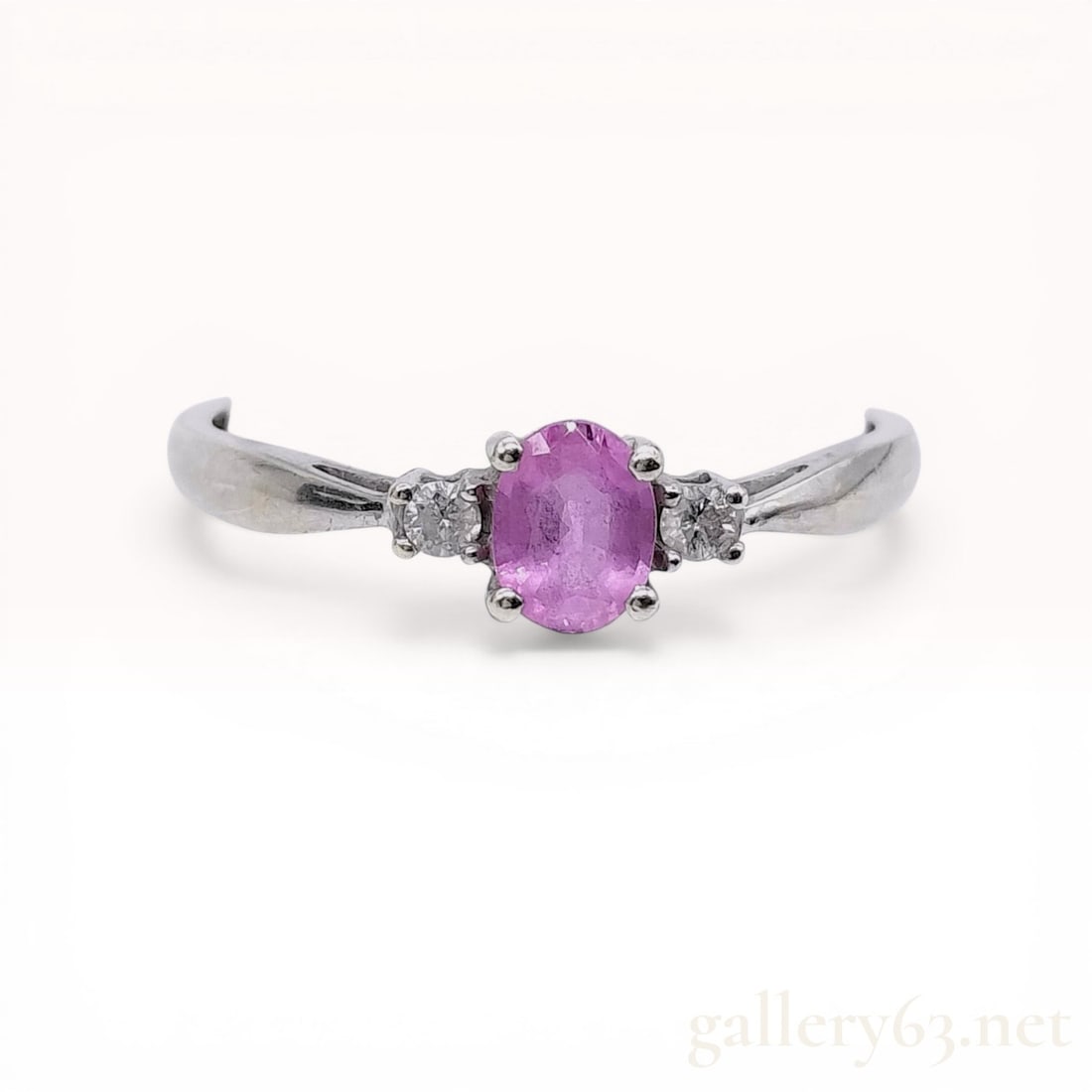 9 Karat White Gold Pink Sapphire and Diamond Trilogy Ring: 9 karat white gold trilogy ring featuring a central oval-cut pink sapphire and two round brilliant-cut diamond accents. The center stone is held in a four-prong setting, while the side diamonds are se