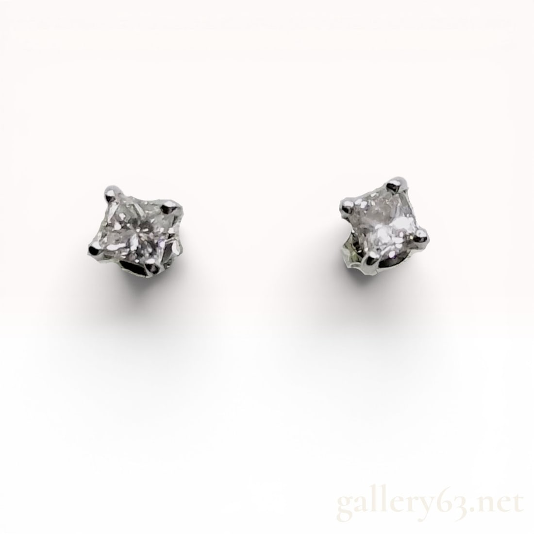 A Pair of Princess Cut Diamond and Platinum Stud Earrings: A matched pair of diamond stud earrings featuring two square princess-cut diamonds set in 900 platinum. Each stone is held in a traditional four-prong basket setting and secured with friction posts an