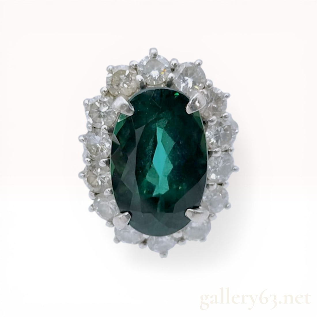 Platinum Chrome Tourmaline and Diamond Halo Cocktail Ring: A platinum cocktail ring featuring a central oval faceted green tourmaline, secured by four double-prongs. The center stone is encircled by a halo of fourteen round brilliant-cut diamonds set in a rai