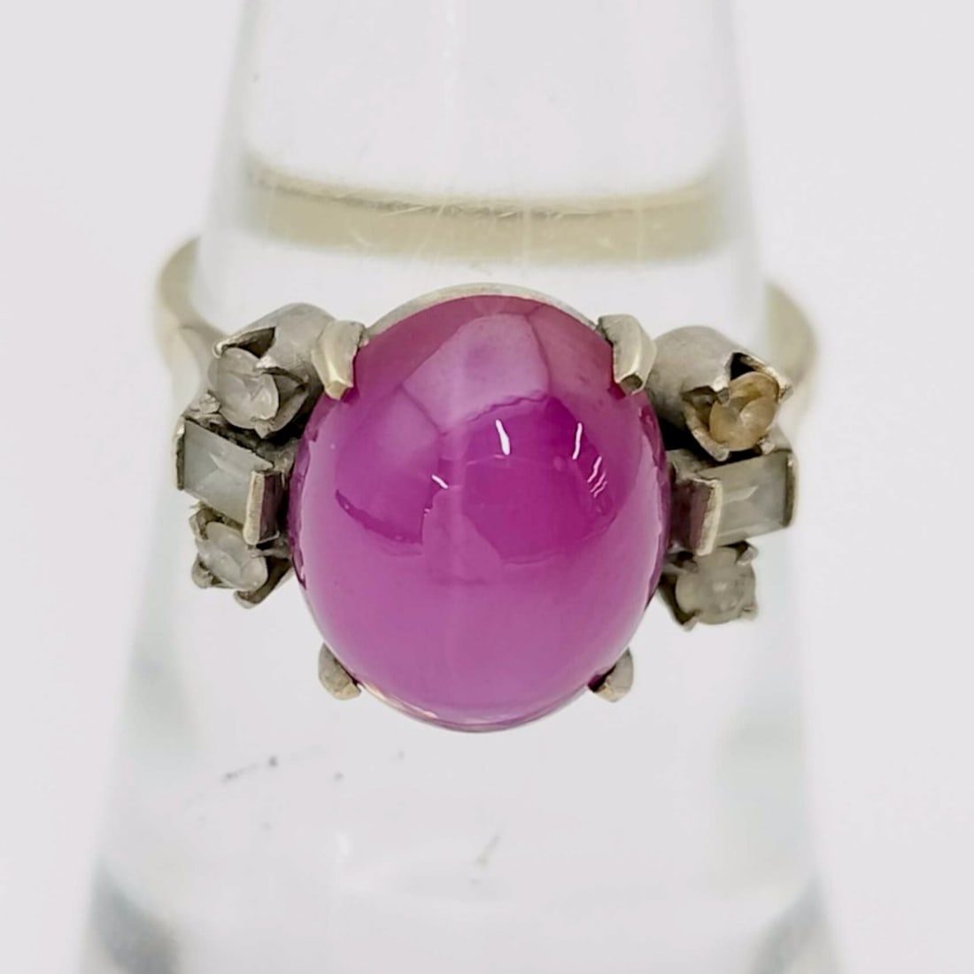 Vintage 14 Karat Two-Tone Gold Star Ruby and Diamond Cocktail Ring: Vintage cocktail ring featuring a central oval purplish-pink star ruby cabochon, mid-20th century. The 14 karat yellow gold shank is joined to a white gold head with tiered shoulders set with four bag