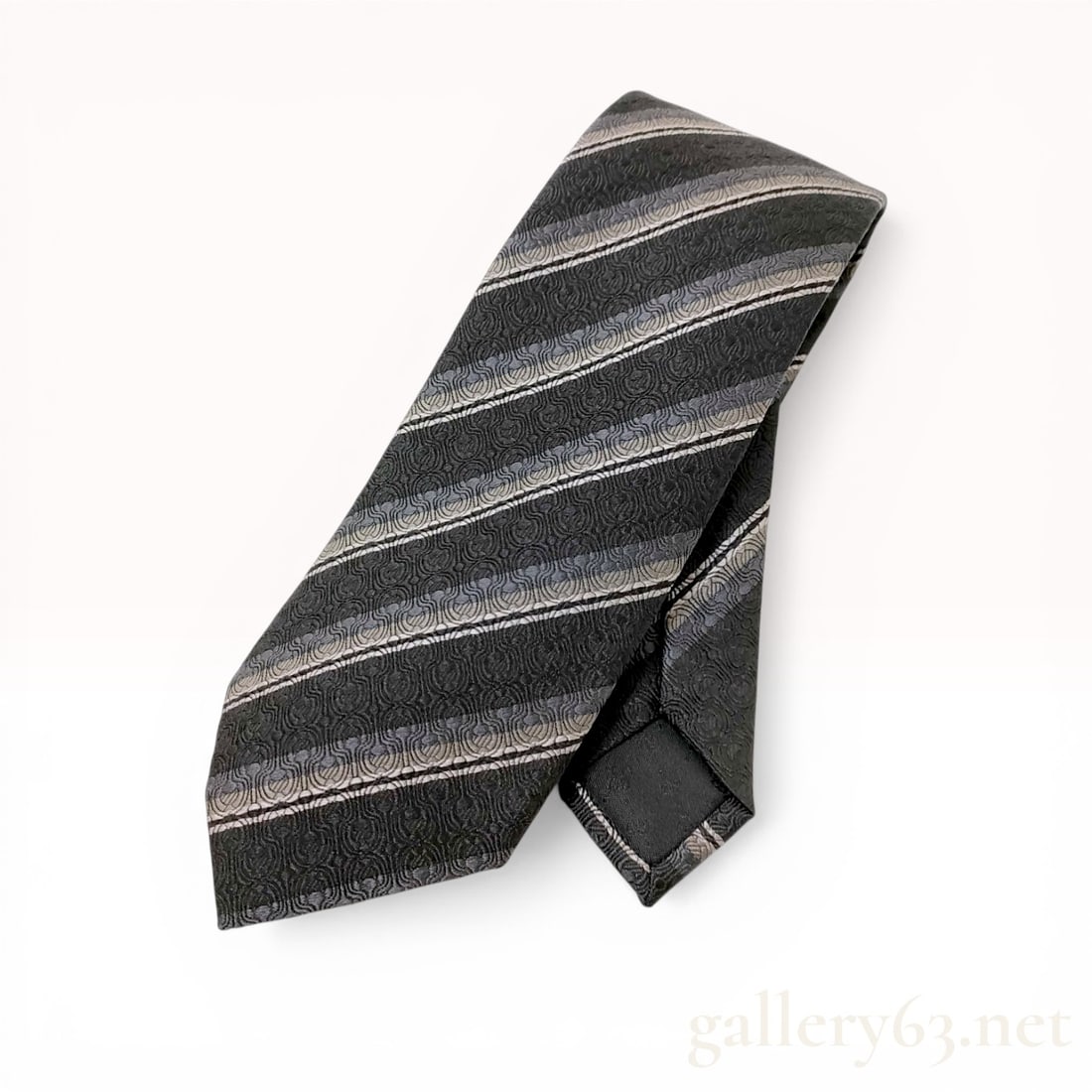 Gucci Striped Silk Jacquard Necktie: Gucci silk jacquard necktie featuring diagonal stripes in shades of black, charcoal, and silver. The textile is constructed with an all-over circular scrollwork jacquard weave. A woven Gucci keeper lo