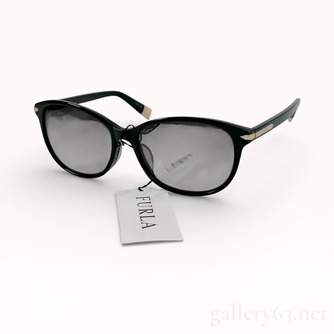 Furla SFU217J Black Acetate Cat-Eye Sunglasses: Furla sunglasses, model SFU217J, featuring a soft cat-eye frame constructed from polished black acetate. The temples are accented with gold-toned metal plaques bearing the brand name and finished with