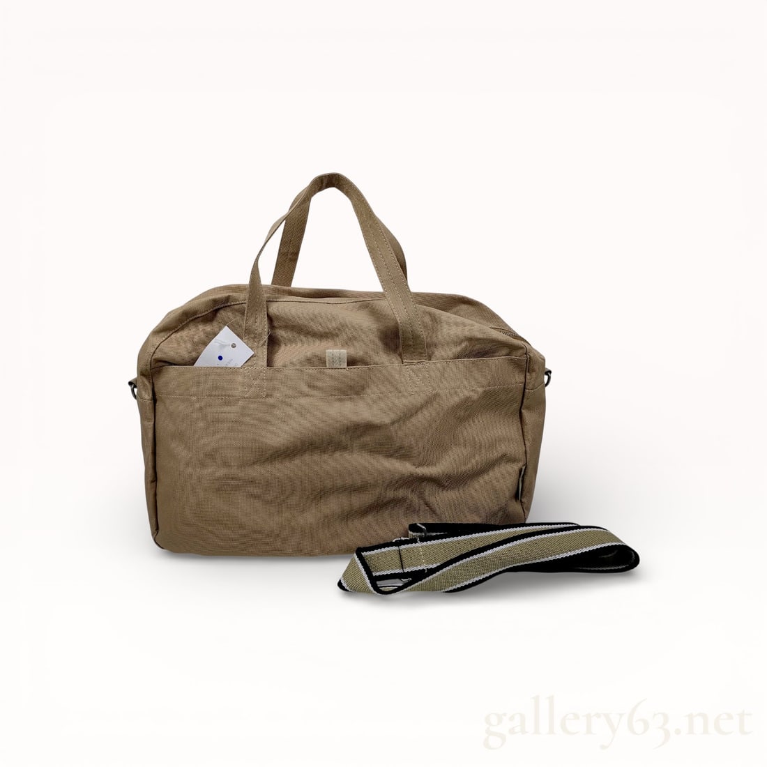 CALPAK Luka Duffel Bag in Tan: CALPAK Luka duffel bag in tan heavyweight canvas. The bag features a synthetic satiny lining, matte silver-tone hardware, and a top zipper closure. It includes a detachable, adjustable striped webbing