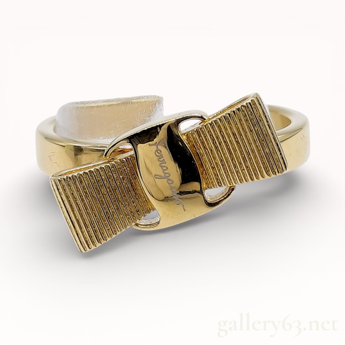 Salvatore Ferragamo Vara Bow Ring in Gold-Tone Metal: Salvatore Ferragamo Vara bow ring featuring the signature house motif with ribbed loops and a smooth central buckle. The piece is crafted from gold-tone metal and features an open-back bypass style sh