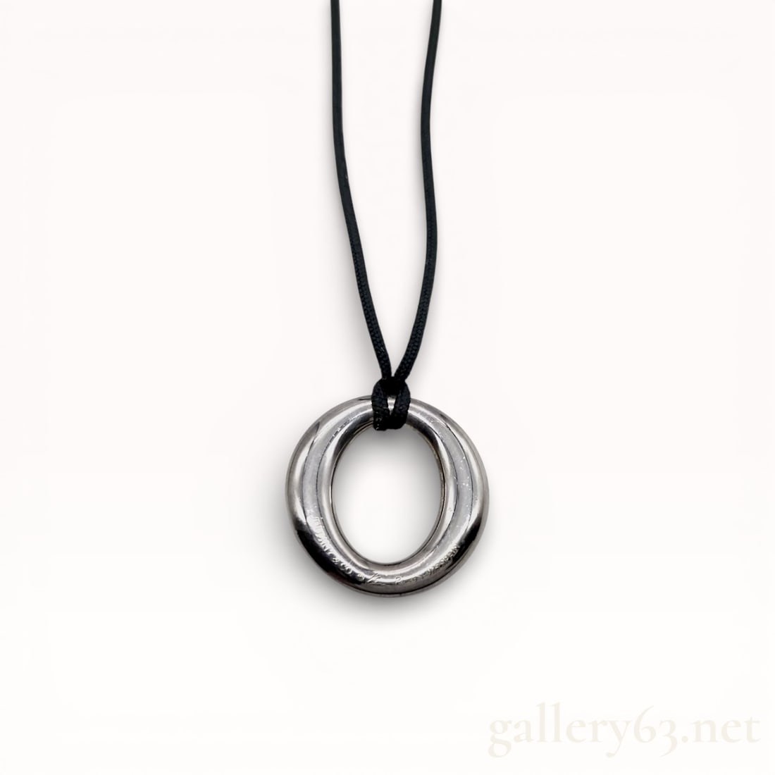Elsa Peretti for Tiffany and Co. Sevillana Sterling Silver Pendant Necklace: Elsa Peretti for Tiffany and Co. Sevillana pendant necklace in sterling silver. The open circle pendant features a smooth, rounded profile and is suspended from a black woven textile cord finished wit