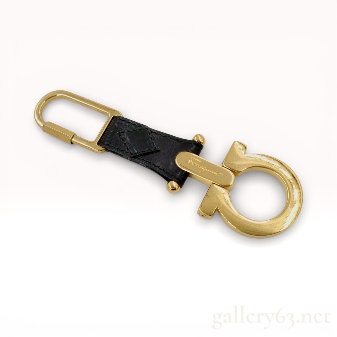 Salvatore Ferragamo Gancini Leather and Gold-Toned Metal Keychain: Salvatore Ferragamo Gancini keychain featuring a black leather strap with a stitched diamond motif. The piece is constructed with gold-toned metal hardware, including a spring-loaded rectangular carab