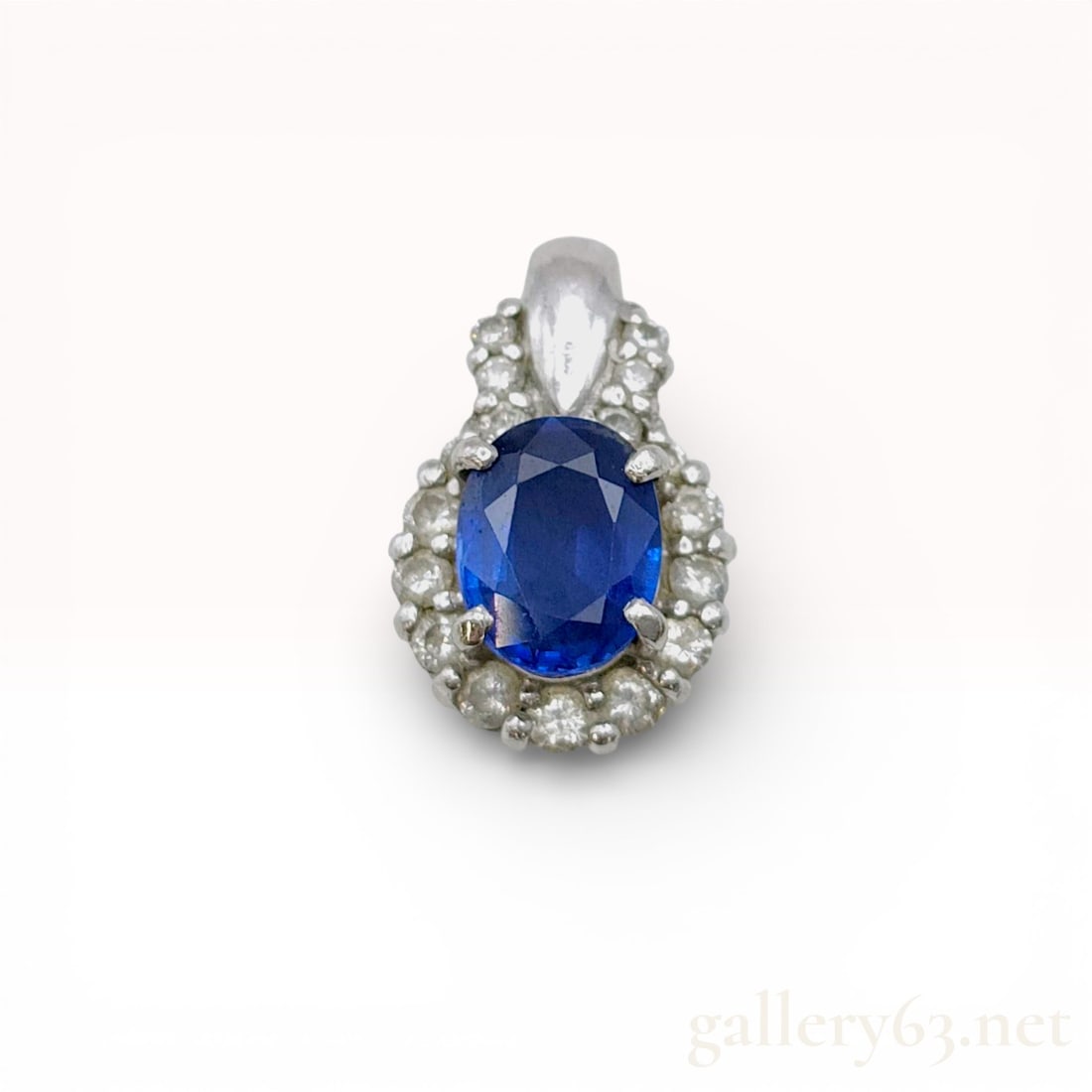 Sapphire and Diamond Halo Pendant in 900 Platinum: A 900 platinum halo pendant featuring a central oval-cut blue sapphire weighing approximately 0.69 carats. The primary stone is surrounded by a border of round brilliant-cut diamonds with further diam