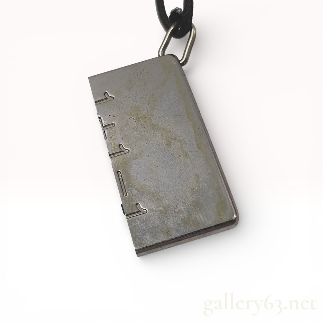 Hermes Silver-Tone Ruler Pendant Necklace: Hermes rectangular tag pendant necklace in a ruler motif, late 20th century. The silver-tone metal pendant features incised graduations along one edge and is suspended from a black braided textile cor