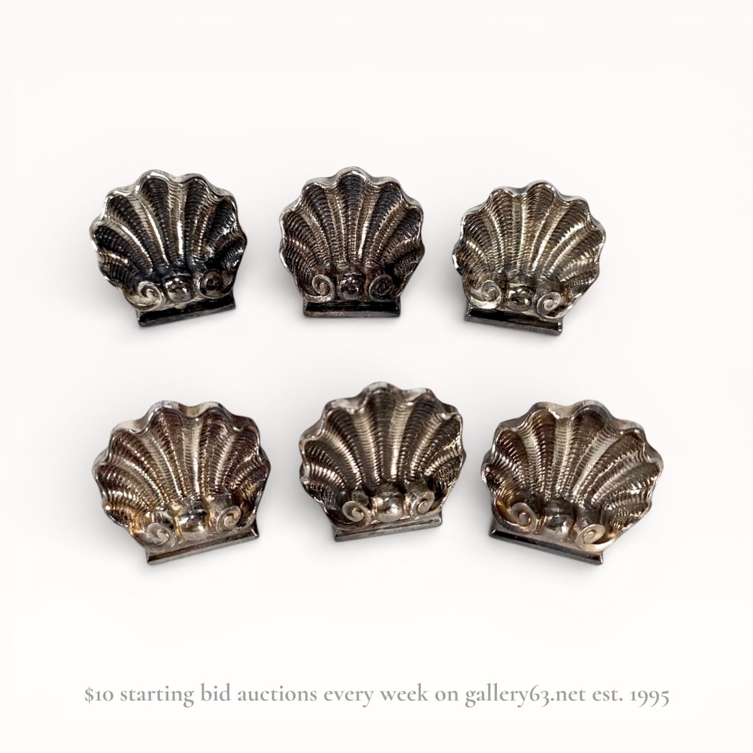 A Set of Six Christofle Silver-Plated Shell-Form Place Card Holders: A set of six silver-plated place card holders by Christofle, France, 20th century. Each holder is modeled as a ribbed scallop shell with a scrolled base and a weighted flat bottom designed to secure c