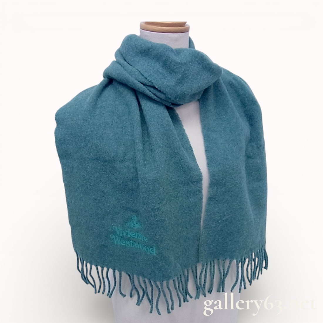 Vivienne Westwood Teal Wool Scarf: Vivienne Westwood wool scarf in a solid teal blue color. The item is constructed from 100% wool and features a tonal embroidered orb logo with the brand name on the lower front. It is finished with tw
