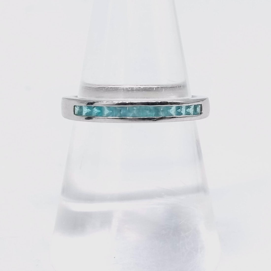 Platinum and Princess Cut Paraiba Tourmaline Channel Set Half Eternity Band: Platinum half eternity band featuring ten channel-set princess cut light blue gemstones. The interior of the band is stamped with Pt950 and 0.30. The gemstones are set in a continuous row across the t