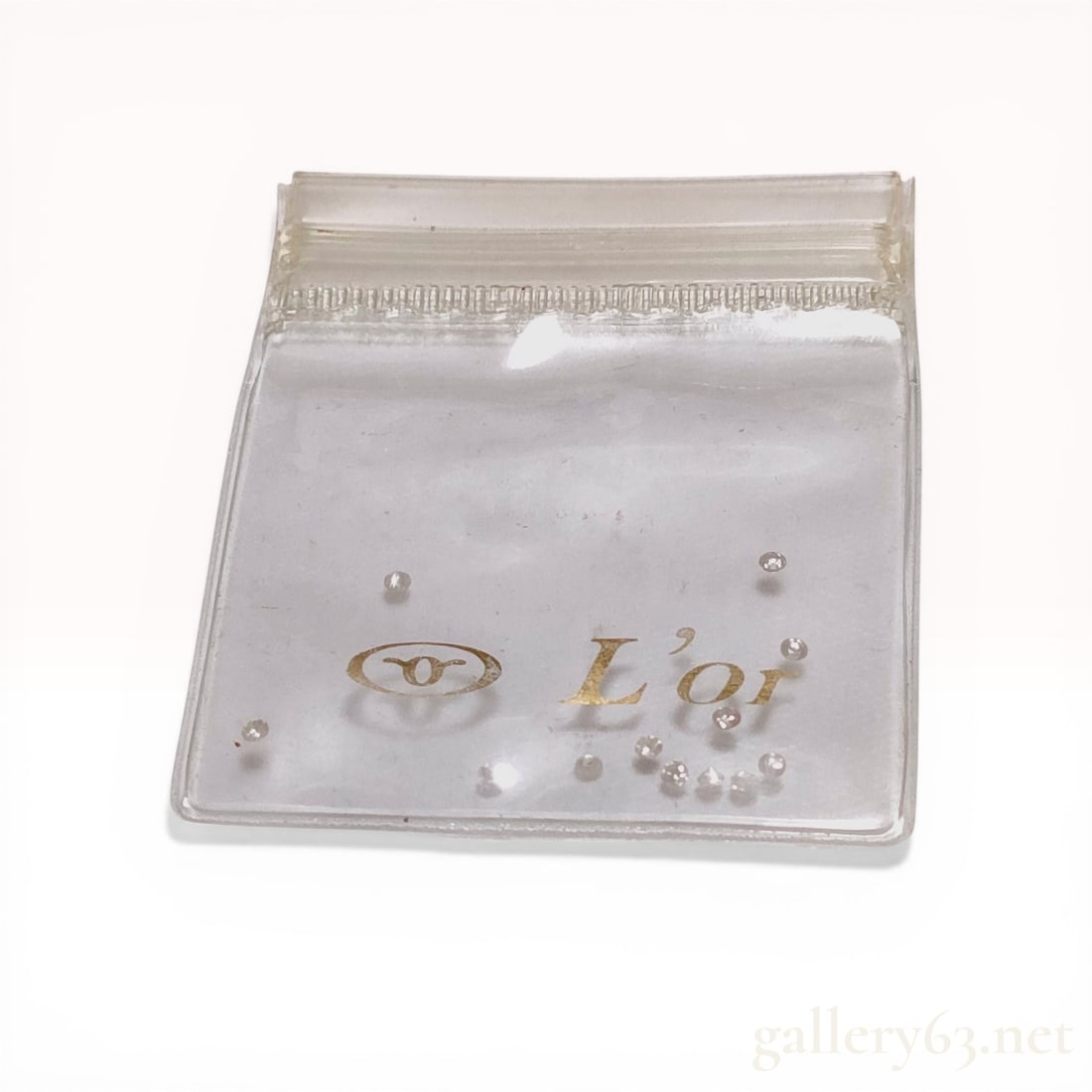 A Collection of Melee Diamonds in a L'or Branded Pouch: A collection of loose melee diamonds presented in a clear plastic pouch with a gold-tone L'or brand mark. The stones appear to be round brilliant cut and range in color from colorless to near-colorles