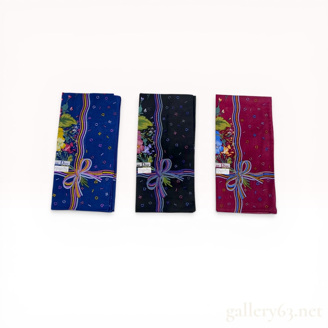 A Trio of Christian Dior Cotton Handkerchiefs in Original Box: Christian Dior set of three cotton handkerchiefs, manufactured under license by Kanebo Dior Co., Ltd. in Japan. Each features a floral border, a wavy multi-colored ribbon stripe with corner bow, and a
