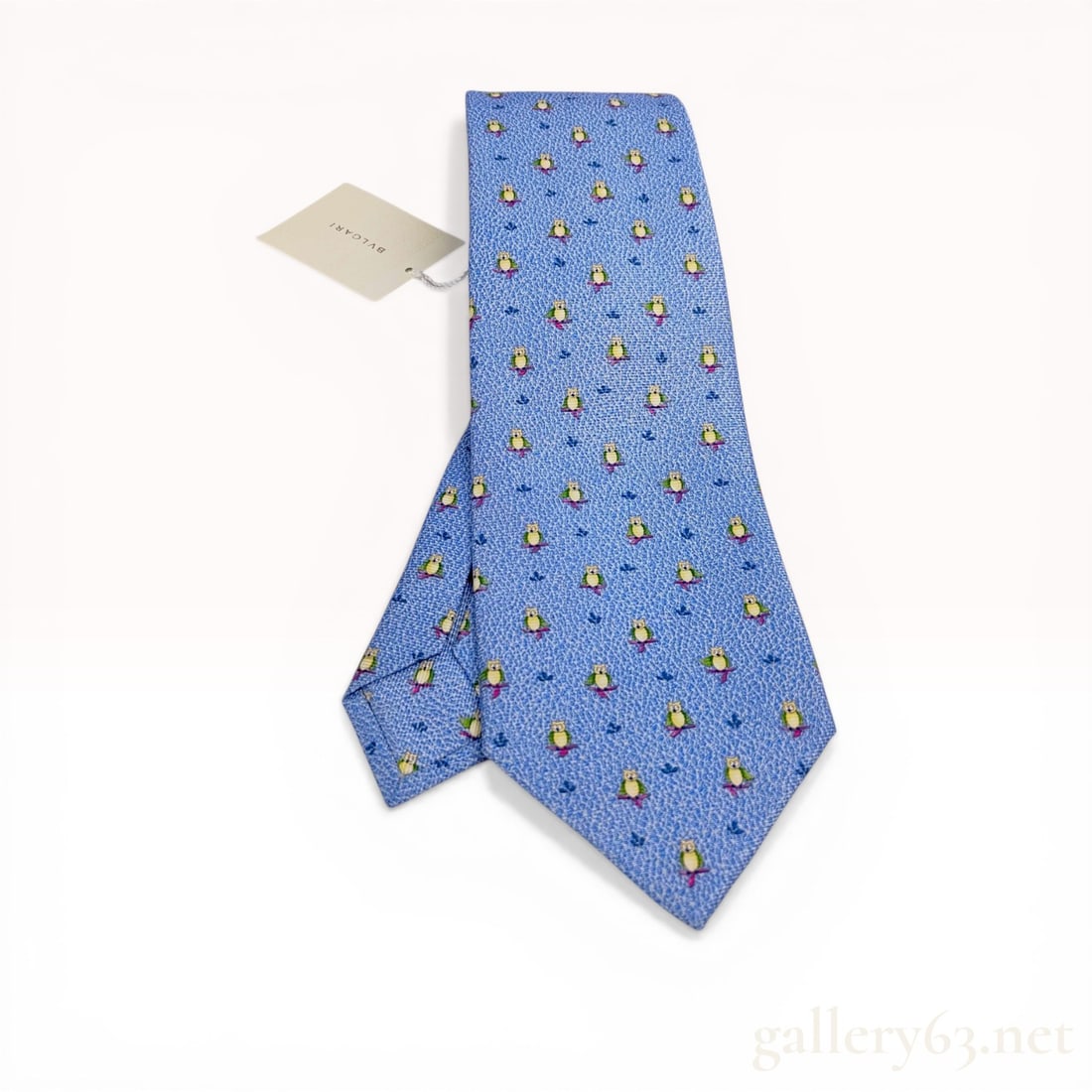 Bvlgari Silk Necktie with Repeating Owl Pattern new with tatgs: Bvlgari silk necktie featuring a repeating whimsical pattern on a light blue ground. The design consists of small owls in shades of green and yellow perched on pink branches, interspersed with navy bl