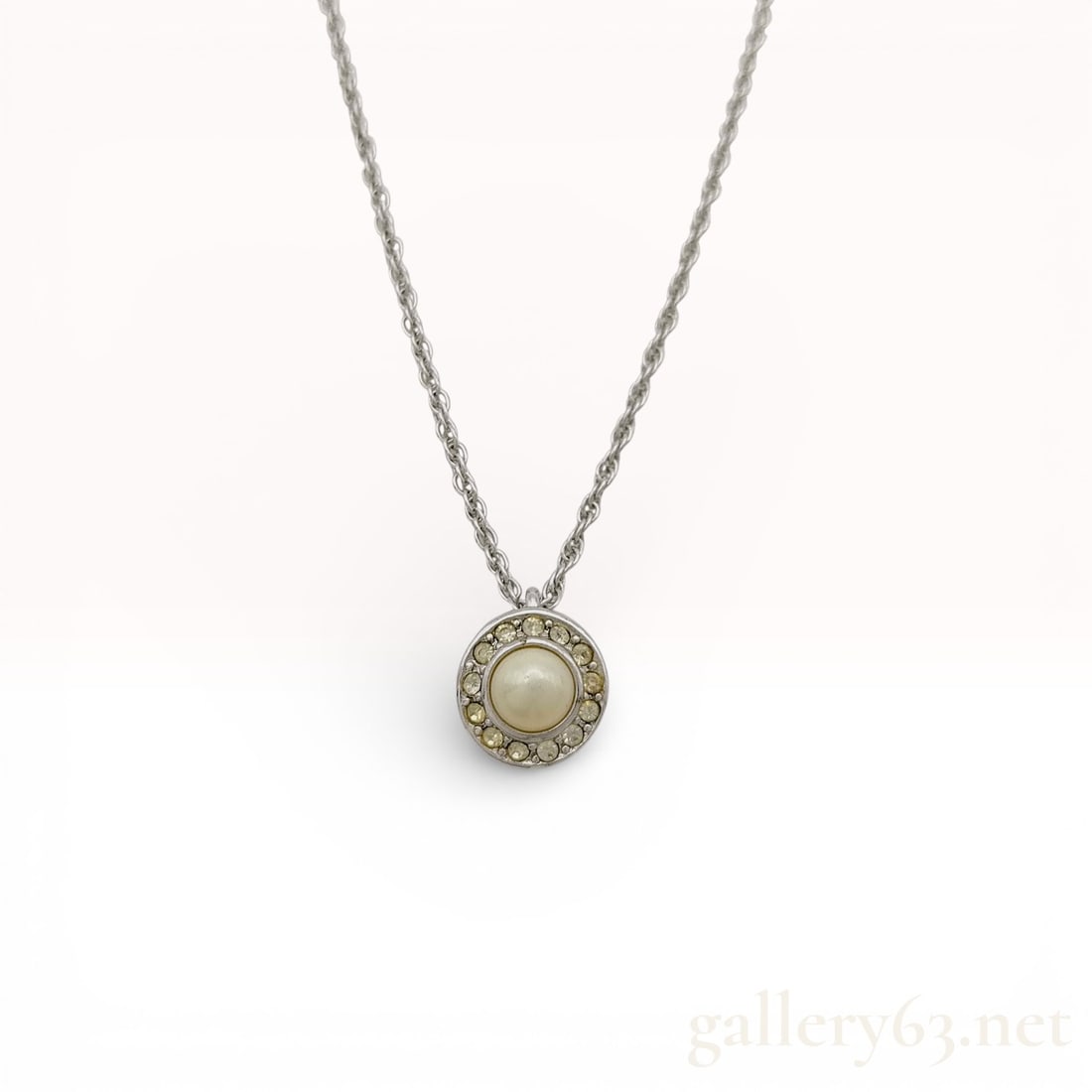 Christian Dior Faux Pearl and Rhinestone Silver-Tone Necklace: A Christian Dior silver-tone necklace featuring a circular pendant set with a central cream-colored faux pearl. The pearl is bordered by a halo of clear rhinestones. The pendant is suspended from a fi