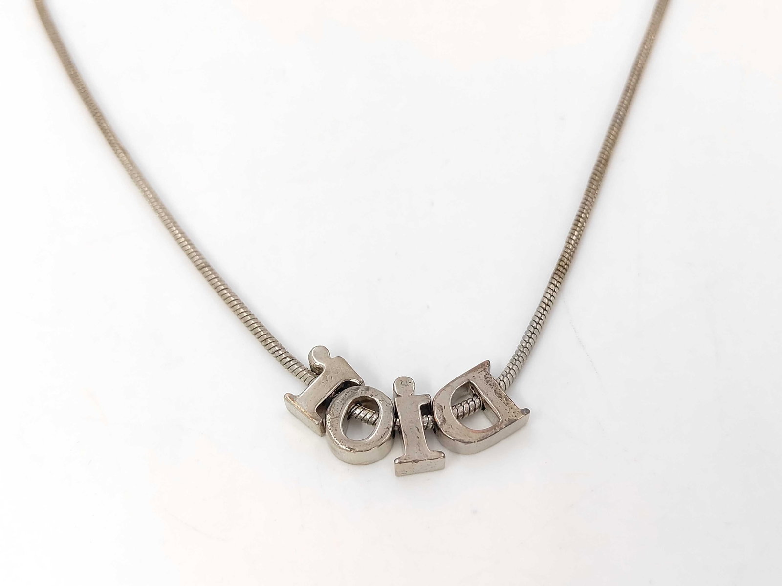 Silver-Tone Snake Chain Necklace with Sliding DIOR Letter Charms: A vintage silver-tone costume metal necklace featuring a fine snake chain. The center of the necklace is adorned with four individual sliding letter charms that spell out DIOR. The piece is secured wi