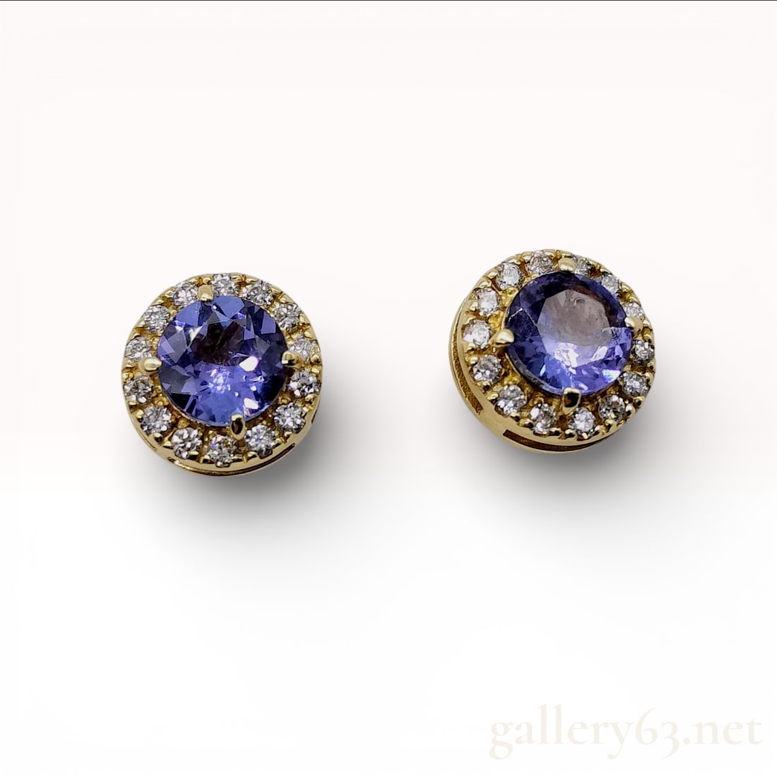 18K Yellow Gold Tanzanite and Diamond Halo Stud Earrings: These 18K yellow gold stud earrings feature a matched pair of natural round mixed-cut tanzanites. Each central stone is surrounded by a halo of round brilliant-cut diamonds. The earrings are secured w