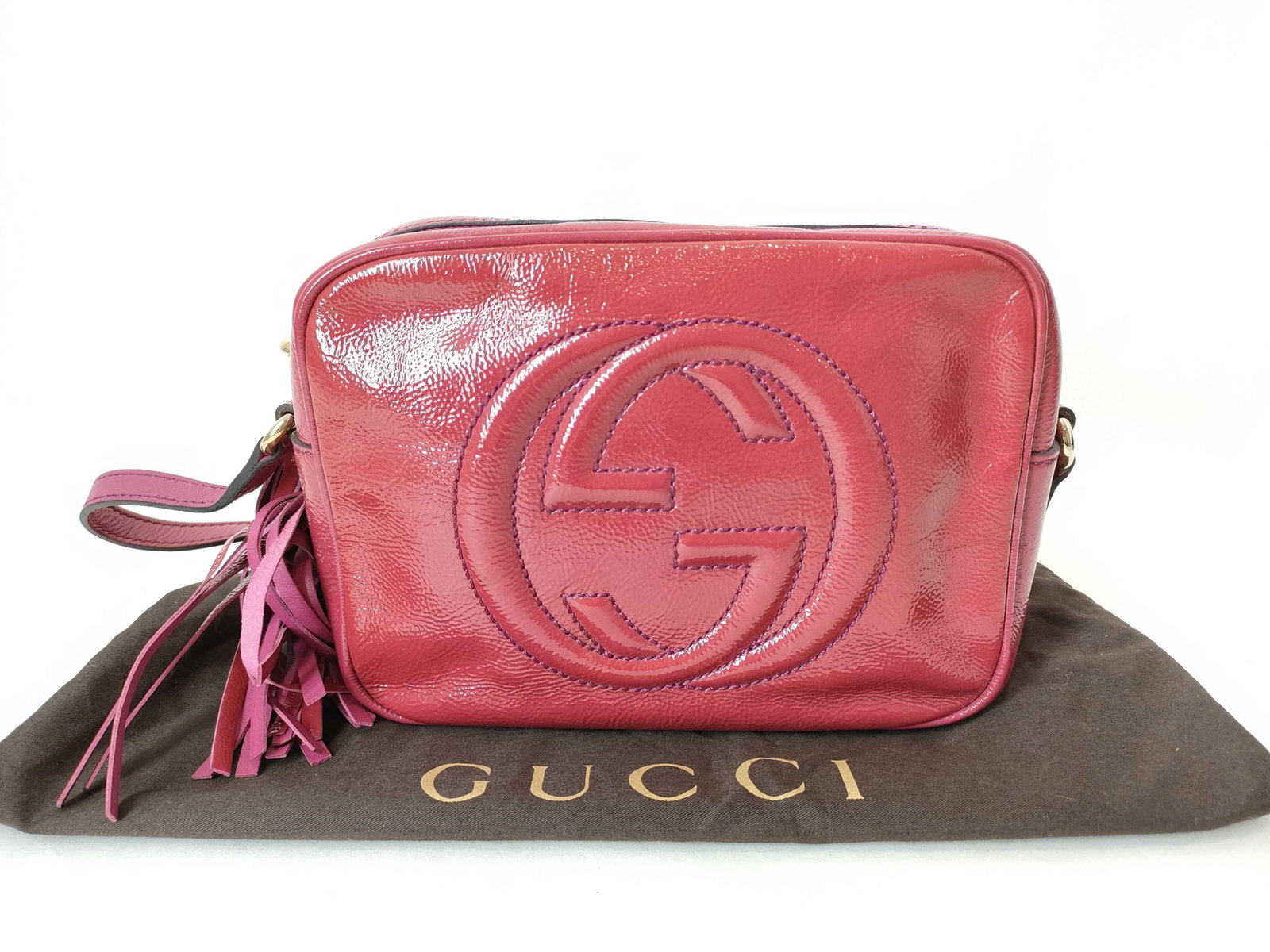 Gucci Soho Disco Bag in Pink Patent Leather: A Gucci Soho Disco crossbody bag crafted from vibrant pink patent leather. This iconic silhouette features the signature embossed interlocking G logo on the front face. The bag is designed with a top 