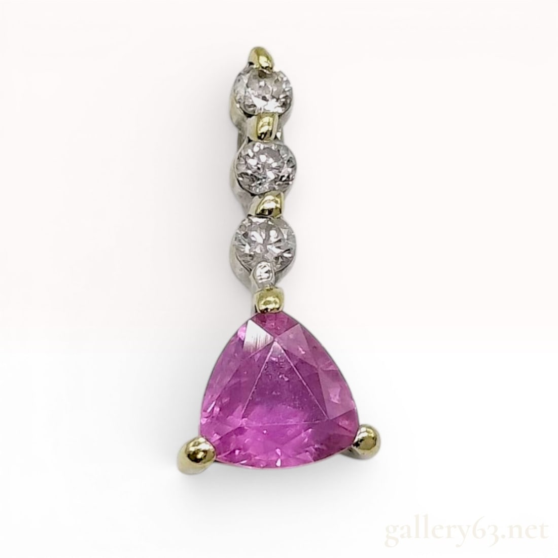 18 Karat White Gold Pink Sapphire and Diamond Drop Pendant: An 18 karat white gold drop pendant featuring a two-tone design with yellow gold accents on the prongs. The pendant is set with a single trillion-cut pink sapphire at the base, held in a three-prong s