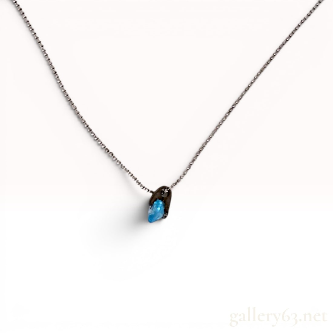 Sterling Silver Ball Chain Necklace with Blue Gemstone Pendant: Sterling silver pendant necklace featuring an organic-form mounting with a dark oxidized finish. The pendant is set with a faceted, translucent bright blue gemstone and is suspended from a fine silver