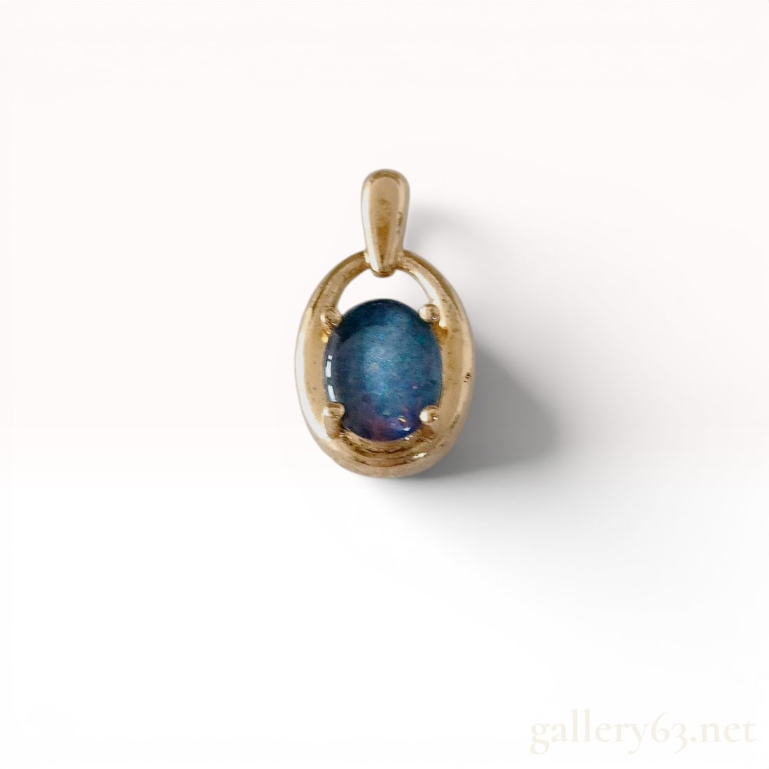 Gold-Plated Sterling Silver and Oval Blue Opal Doublet Pendant: Contemporary openwork oval pendant crafted in gold-plated sterling silver. The design features a central prong-set oval cabochon blue opal doublet displaying blue and violet play-of-color within an op