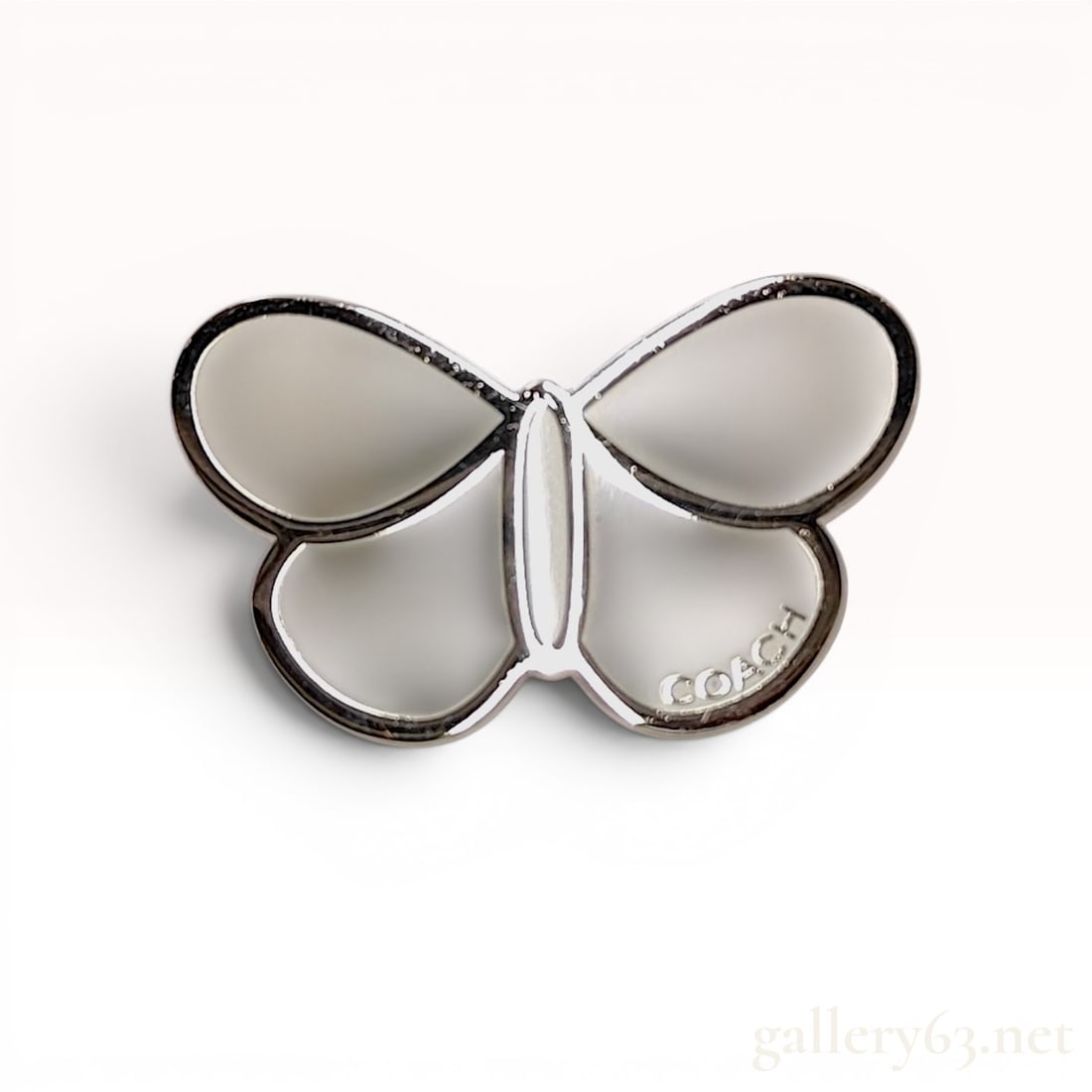 Coach Enamel Butterfly Lapel Pin: Coach designer butterfly lapel pin featuring a stylized four-section wing design. The wings are filled with cream-colored enamel and outlined in polished silver-tone metal, with the brand name debosse
