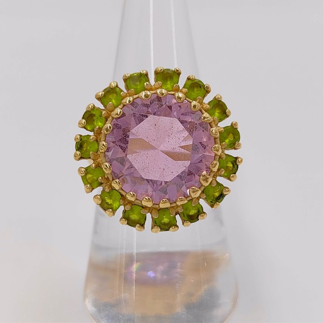 Kate Spade New York Gold-Toned Pink and Green Stone Cocktail Ring: Kate Spade New York floral-inspired cocktail ring. The design features a large, round-faceted lavender center stone held in a multi-prong crown setting, encircled by a halo of sixteen round-faceted li