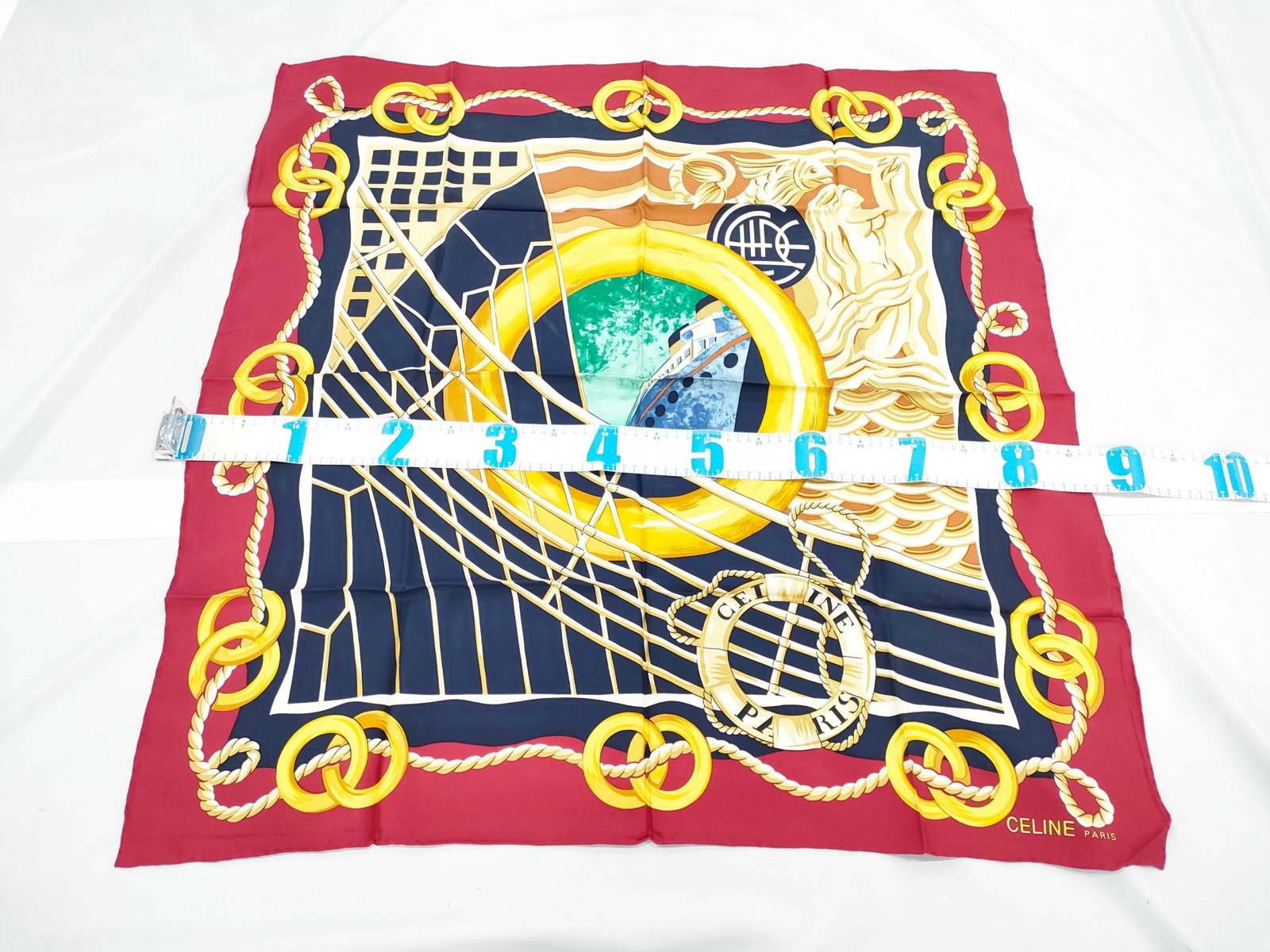 Celine Paris Nautical Graphic Print Silk Twill Scarf: A vintage square silk twill scarf by Celine Paris featuring a complex nautical graphic design. The central motif depicts a stylized ocean liner viewed through a circular gold porthole. This is surroun
