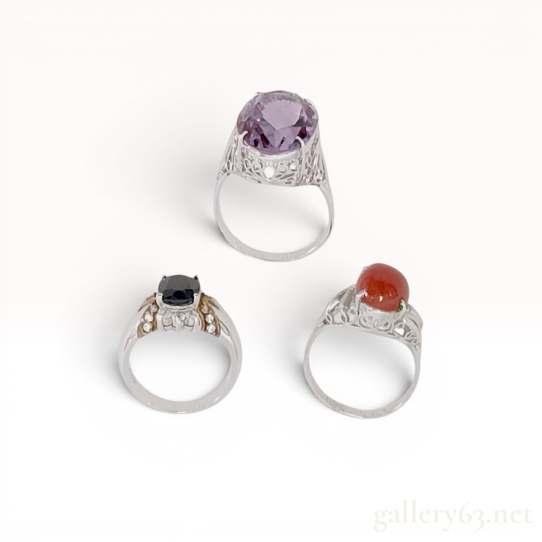 Three Vintage Gemstone and Sterling Silver Rings: Trio of vintage-style gemstone rings featuring an amethyst-colored faceted stone, a black stone with 24 karat gold-plated accents, and a red-orange cabochon. Settings include high-profile filigree gal