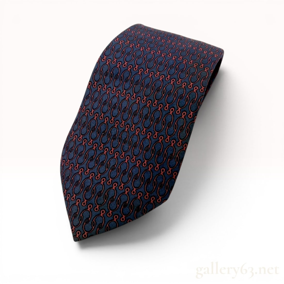 Hermes Navy Silk Necktie with Red Horse-Bit Pattern 733 FA: Hermès silk necktie featuring a repeating interlocking horse-bit motif in red and black on a navy ground. Constructed in France from 100% silk with a traditional pointed blade. Features a print