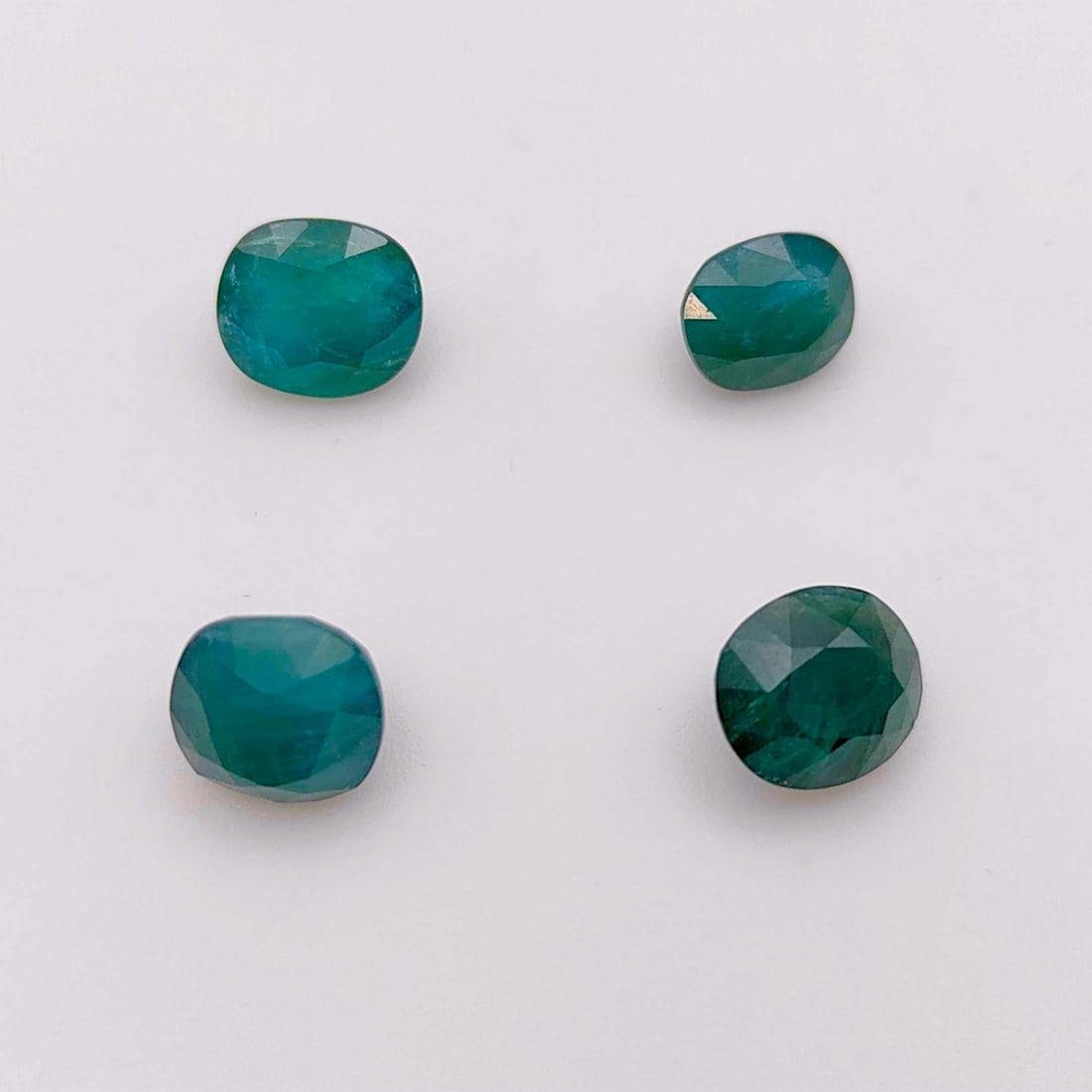Four Natural Faceted Grandidierite Gemstones with Central Gem Laboratory Reports: This collection includes four loose faceted gemstones identified as natural grandidierite. Each stone is characterized by a greenish-blue color and a translucent to semi-transparent clarity. The gemst