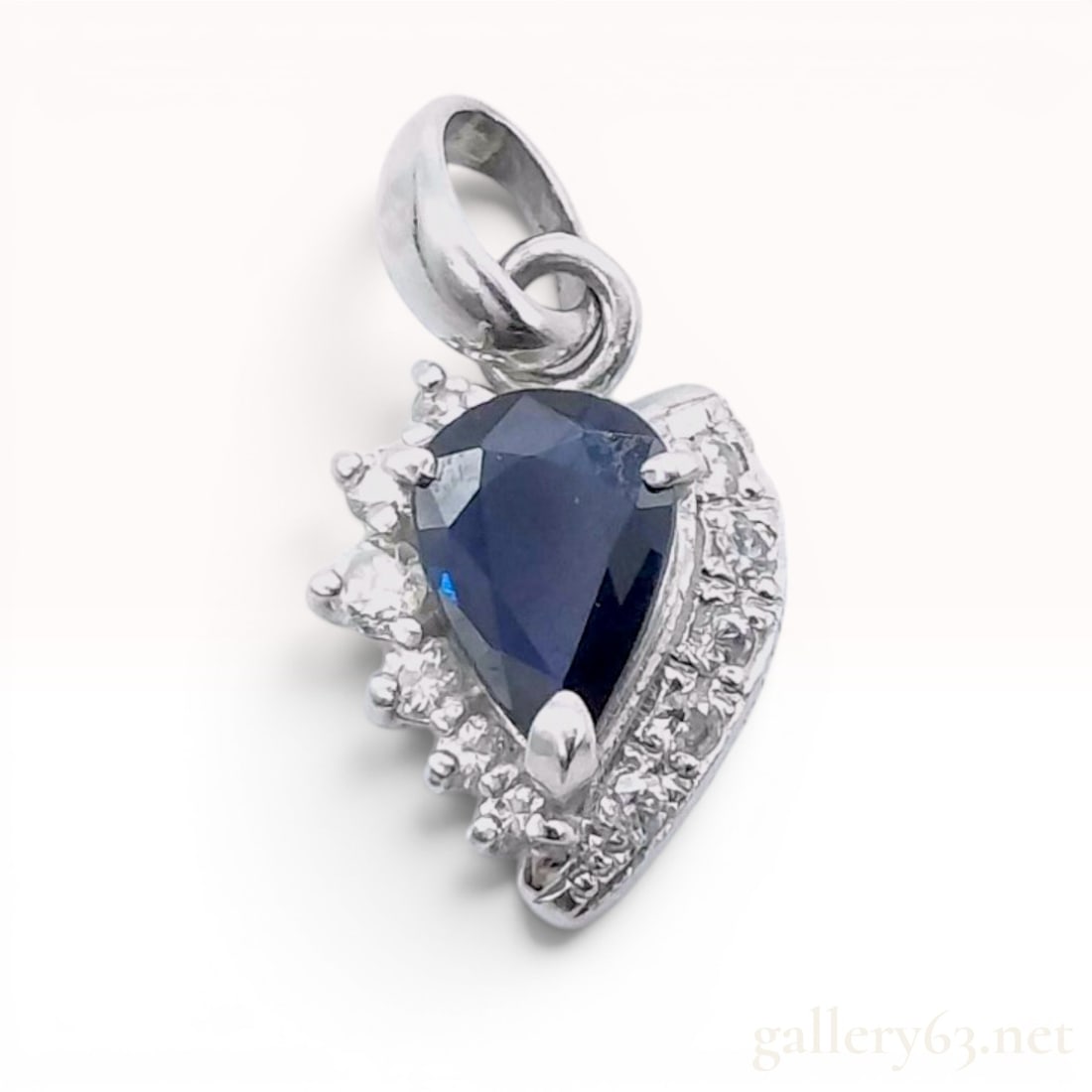 Platinum Pear-Cut Sapphire and Diamond Cluster Pendant: Platinum pendant featuring a central pear-cut blue sapphire accented by a curved, tiered cluster of round brilliant-cut diamonds. The asymmetrical design incorporates a polished edge on one side and a