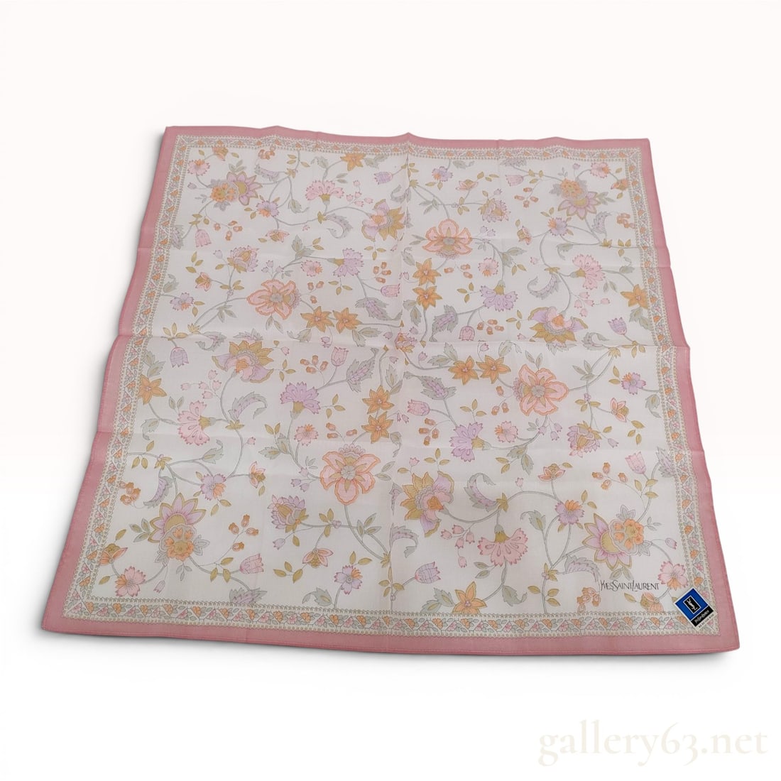 Yves Saint Laurent Floral Print Cotton Pocket Square: Yves Saint Laurent pocket square featuring a pastel floral blossom and vine motif on a white ground with a decorative border and solid pink edges. The textile is made of 100 percent cotton with machin
