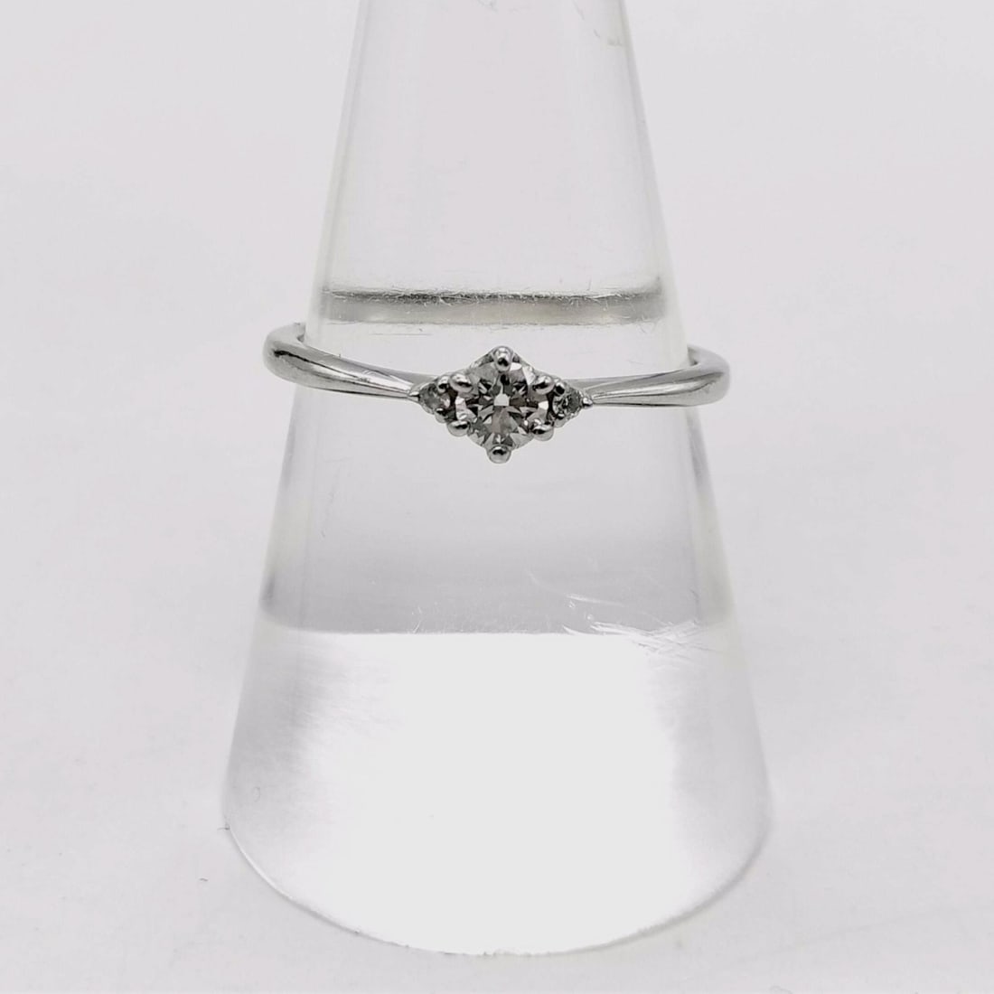 Platinum and Diamond Three-Stone Ring: A platinum ring featuring a center round brilliant cut diamond flanked by two small round accent stones. The diamonds are prong-set on a tapered band with a four-prong mount for the primary stone. Int