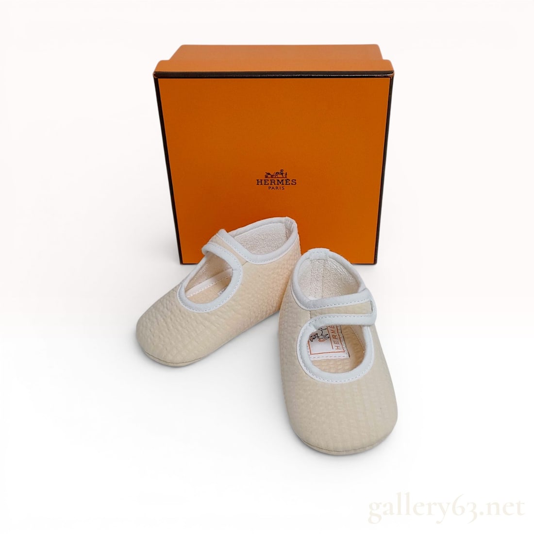 A Pair of Hermes Pif Cabriole Baby Booties with Original Box: A pair of Hermes Pif Cabriole baby booties in a Mary Jane style. The uppers are composed of a cream-colored, texturized seersucker fabric with white piping at the edges. Each bootie has a single strap