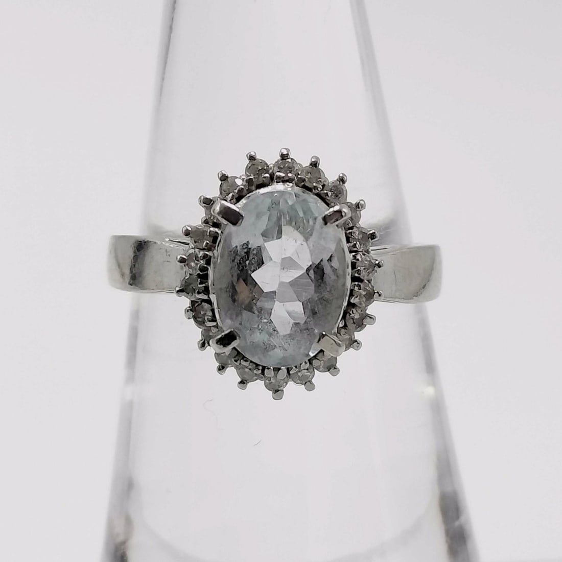 Platinum 1.85ct Aquamarine and .21ctw Diamond Halo Cocktail Ring: This platinum cocktail ring features an oval-cut light blue aquamarine mounted in a four-prong basket setting. The center stone is encircled by a halo of small round-cut accent diamonds in shared-pron