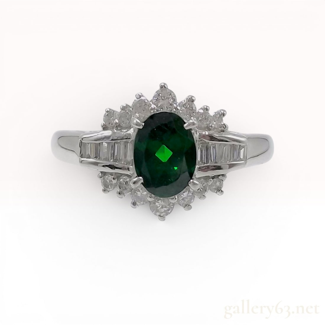 Platinum, Green Garnet, and Diamond Cluster Ring: This platinum cocktail ring features a centrally mounted oval-cut green garnet secured in a four-prong setting. The center stone is surrounded by a tiered halo of round brilliant-cut diamonds. The sho