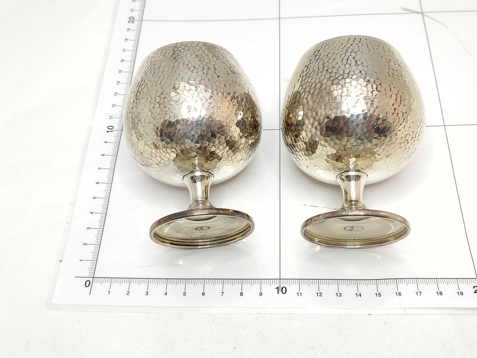A Pair of Hammered Silver Brandy Goblets with Gold-Wash Interiors: A pair of mid-20th-century silver brandy goblets featuring a martelé hammered exterior. The bulbous forms are elevated on short flared stems and circular feet, with the interior bowls finished 