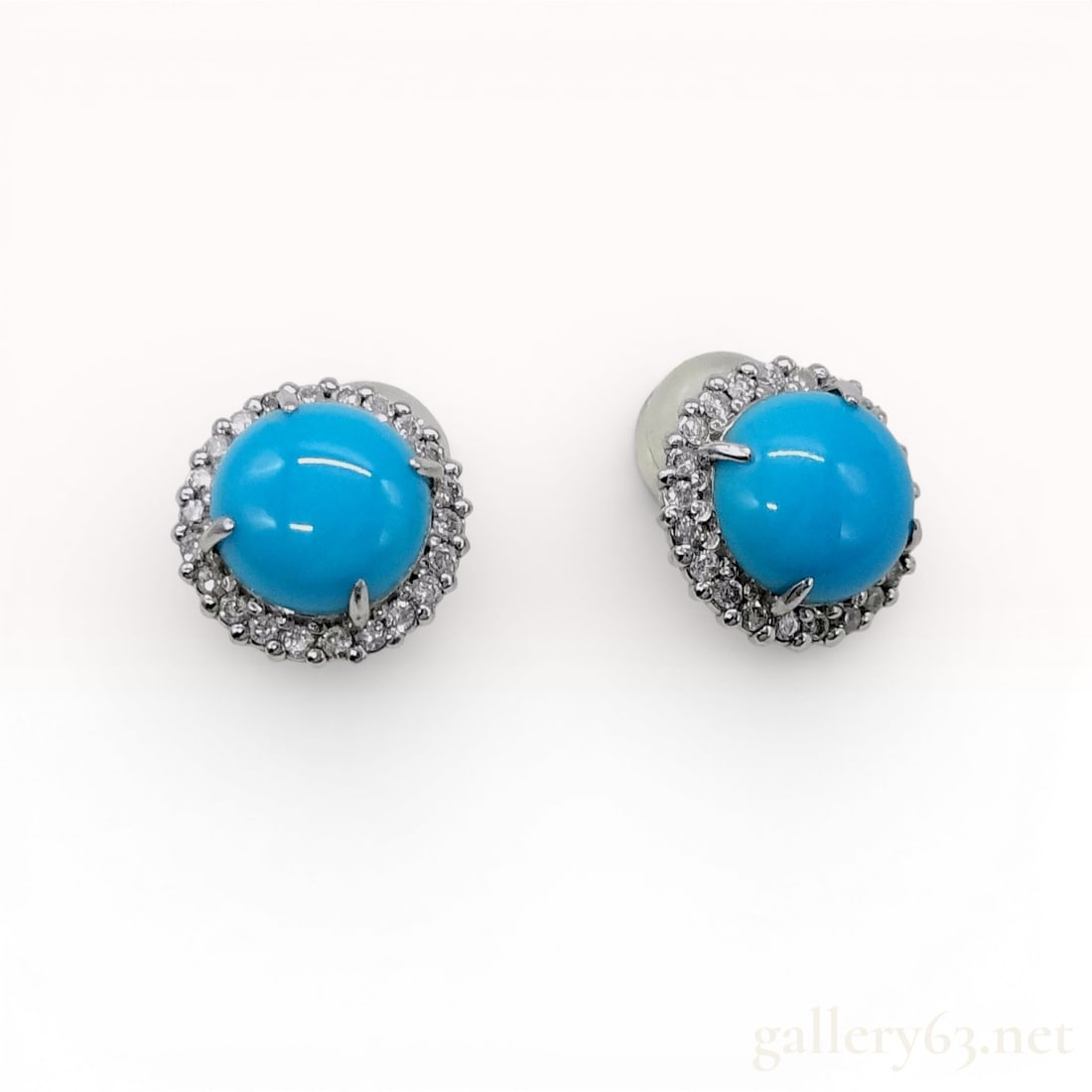 A Pair of Turquoise and Diamond Halo Stud Earrings in 900 Platinum: This is a matched pair of gemstone stud earrings. Each earring is centered with a round cabochon-cut turquoise featuring a vibrant robin's egg blue color and no visible matrix. The center stones are h