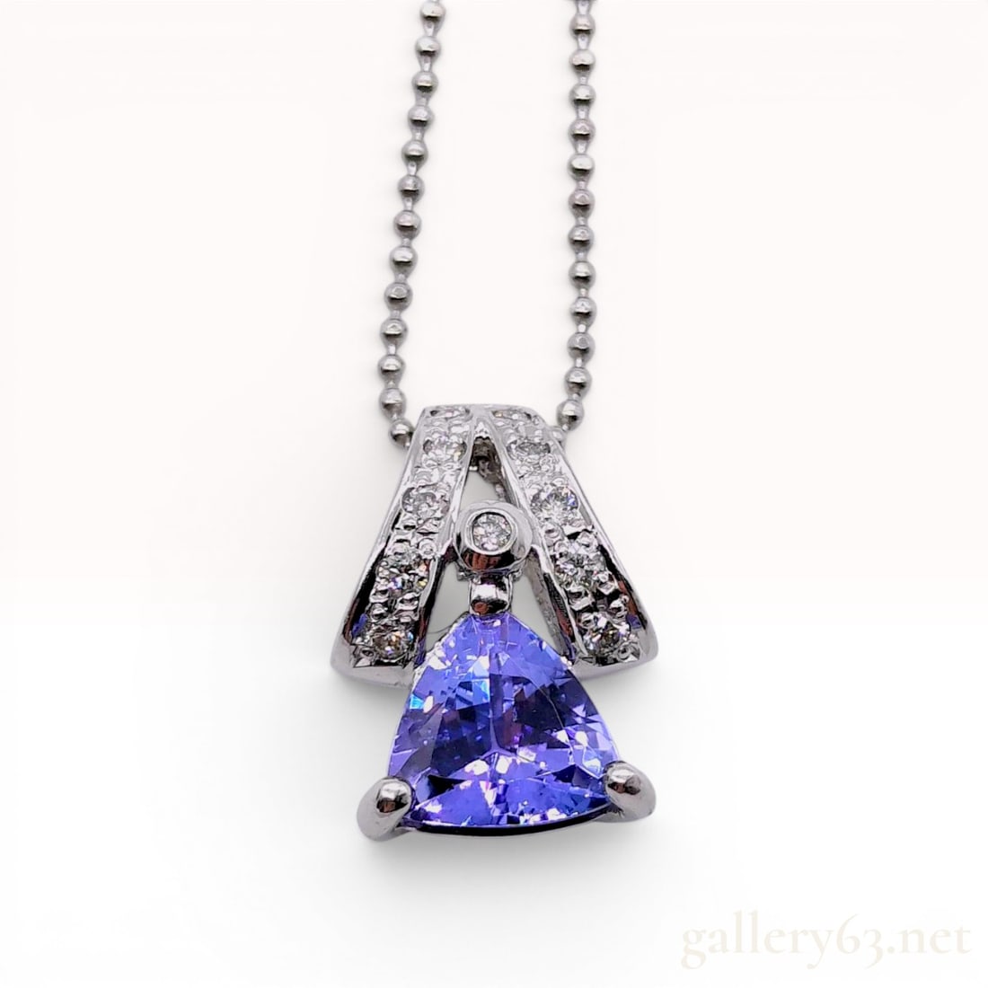 Platinum Tanzanite and Diamond Pendant Necklace: A platinum pendant necklace featuring a trillion-cut violet-blue tanzanite. The pendant reverse is inscribed 1.28, which corresponds to the carat weight of the tanzanite. The bail and central decorati