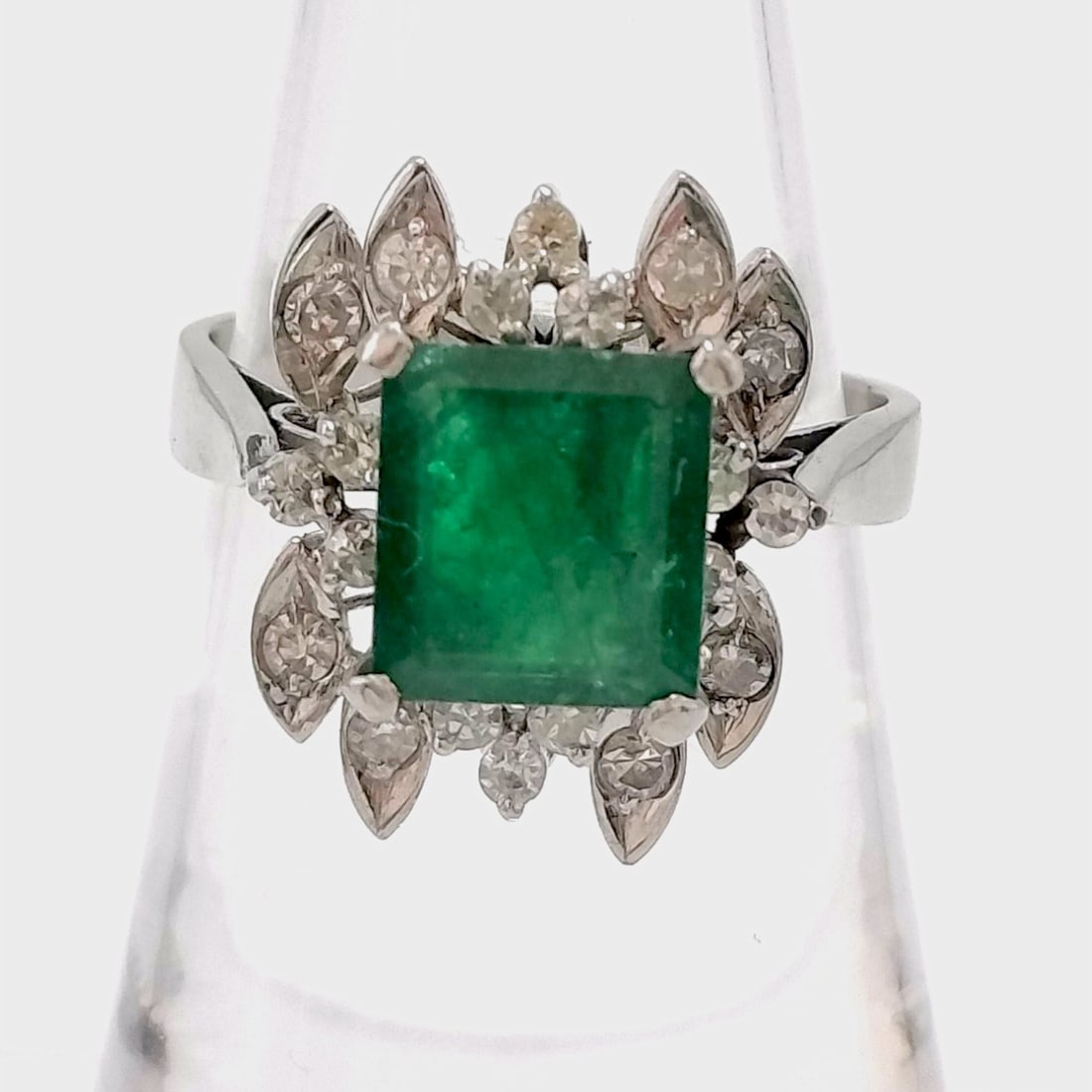Vintage Platinum Emerald and Diamond Cluster Cocktail Ring: A vintage platinum cocktail ring featuring a rectangular emerald-cut emerald as the center stone. The emerald is secured in a four-prong corner setting and displays characteristic natural inclusions. 
