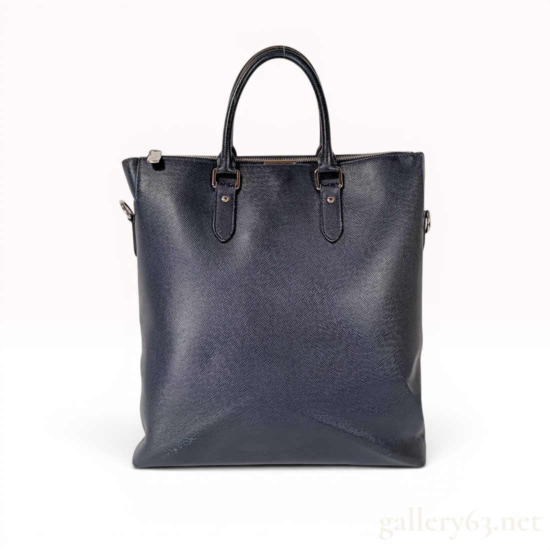 Louis Vuitton Taiga Leather Anton Tote in Dark Navy Blue: Louis Vuitton Anton Tote crafted from dark navy blue Taiga leather with silver-tone hardware. This vertical tote features dual flat top handles, a full-length exterior front pocket, and a single zippe