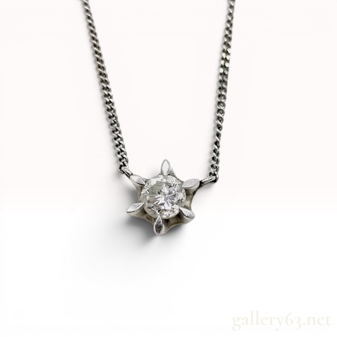 Platinum Diamond Solitaire Starburst Pendant Necklace: Platinum necklace with a starburst-motif pendant featuring a centrally set round brilliant-cut diamond. The pendant is suspended from a fine curb link chain secured with a spring ring clasp. Visible m